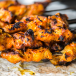 Freshly grilled chicken tikka masala kebabs on skewers dripping onto a piece of naan flatbread cooked in a Tandoori oven.