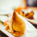 Two white plates containing freshly made samosas, a favorite of Indian cuisine.